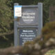 Sign at the entrance of Hockinson Meadows Community Park with 'Welcome' and park regulations text, set among trees.