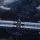 Futuristic space station with twin parallel modules connected in the center, hovering above a dark, forested planet surface at dusk.