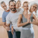 Group of adults in a fitness class standing in a line; front woman in gray with hands in prayer pose.