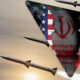 Missiles fly past a triangular opening showing Iran's flag colors and emblem against a sunset sky.