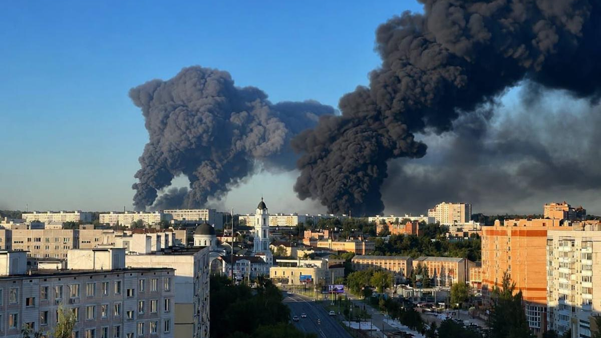 City skyline with enormous black smoke plumes rising from a distant fire across the horizon.