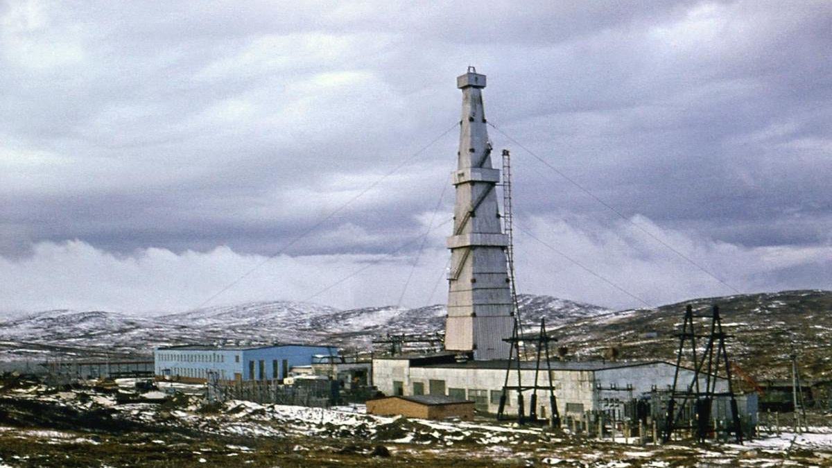 Tall lattice communications tower rising beside blue industrial buildings in a snow-dusted, barren landscape.