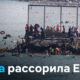 Crowded rocky shoreline with many swimmers near a fenced seawall; DW logo in top-left corner.