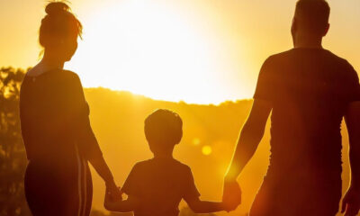 Silhouetted family of three (mother, child, father) holding hands at sunset