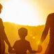 Silhouetted family of three (mother, child, father) holding hands at sunset