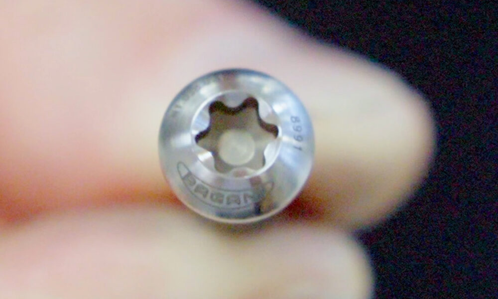 Close-up of a small silver Torx screw head held by fingers, showing the star-shaped recess.