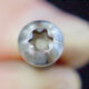 Close-up of a small silver Torx screw head held by fingers, showing the star-shaped recess.