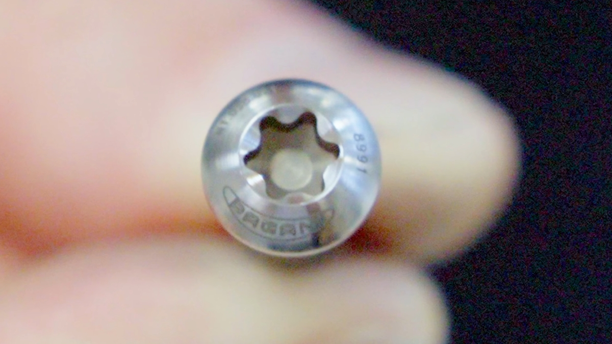 Close-up of a small silver Torx screw head held by fingers, showing the star-shaped recess.