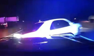White car involved in a nighttime crash with blue emergency lights flashing in the background.
