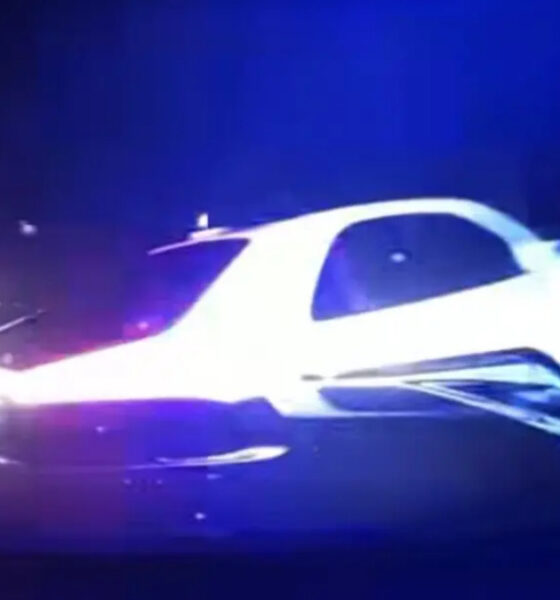 White car involved in a nighttime crash with blue emergency lights flashing in the background.