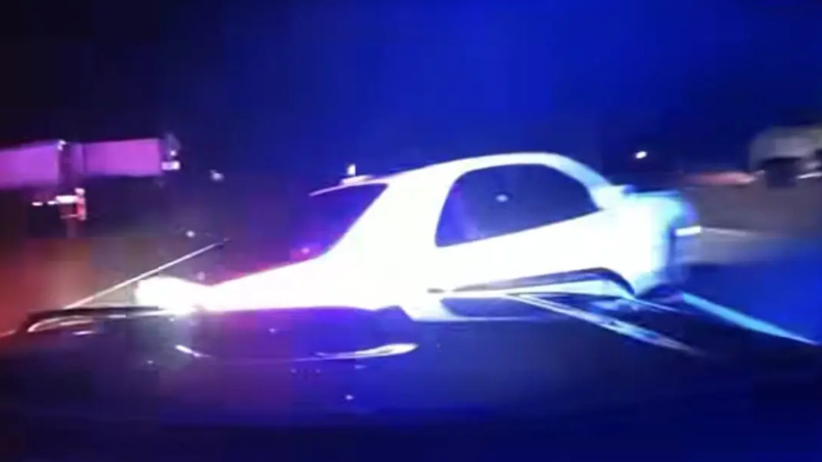 White car involved in a nighttime crash with blue emergency lights flashing in the background.
