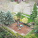 Aerial view of a small playground with a wooden structure and blue slide surrounded by mulch and benches under trees in a residential yard
