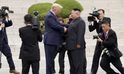 Two world leaders shake hands while photographers film from all sides on a stone staircase.