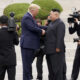 Two world leaders shake hands while photographers film from all sides on a stone staircase.