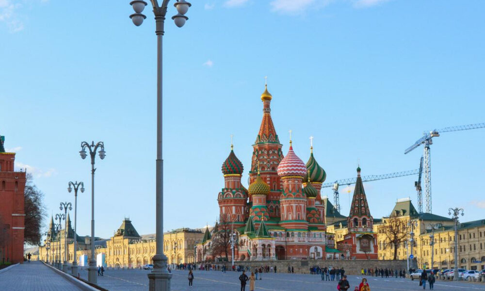 Colorful Saint Basil's Cathedral with onion domes in Red Square, Moscow, crowded plaza in foreground and construction cranes in the background.