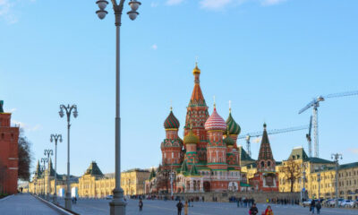 Colorful Saint Basil's Cathedral with onion domes in Red Square, Moscow, crowded plaza in foreground and construction cranes in the background.