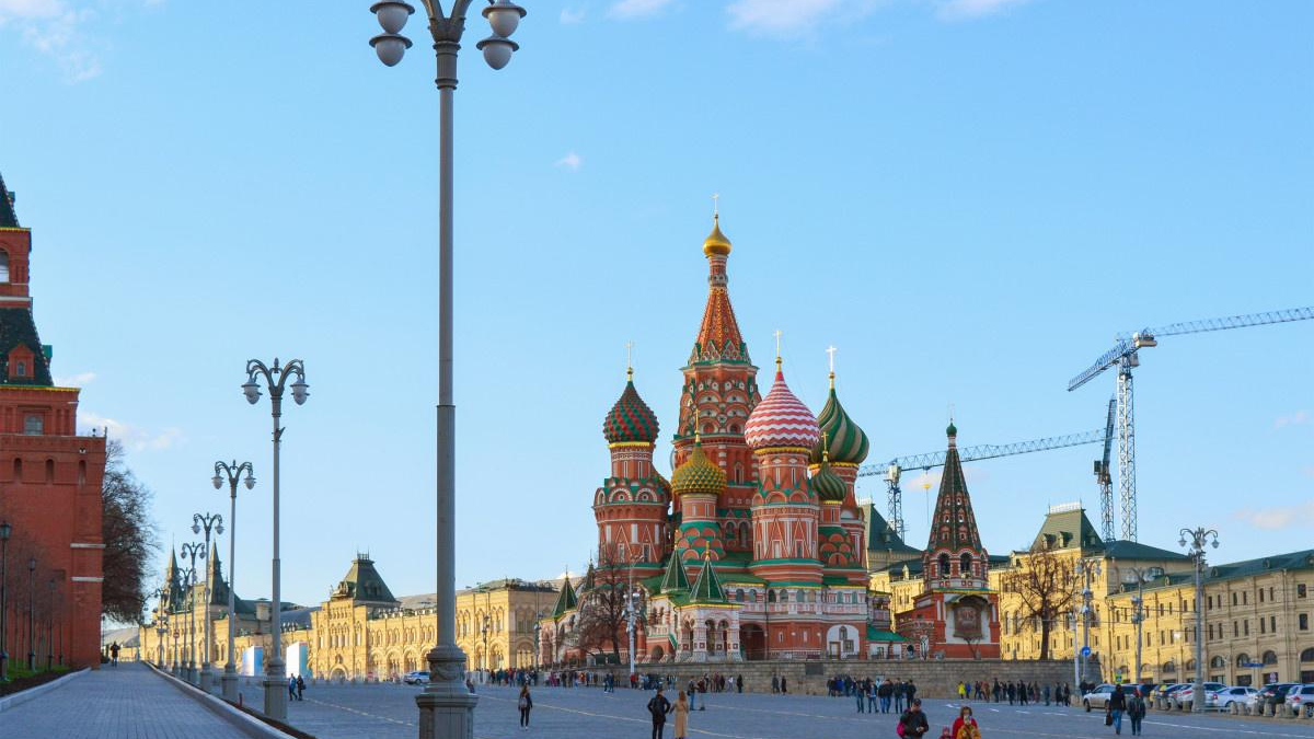 Colorful Saint Basil's Cathedral with onion domes in Red Square, Moscow, crowded plaza in foreground and construction cranes in the background.