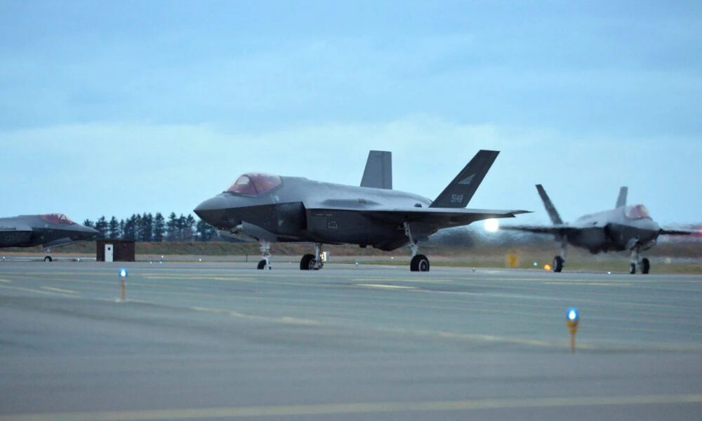 Two gray F-22 fighter jets parked on a runway at an airbase under a blue cloudy sky.