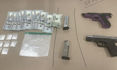 Assorted illegal drugs in small bags, a pile of cash, and two handguns on a brown surface (drug paraphernalia in view).
