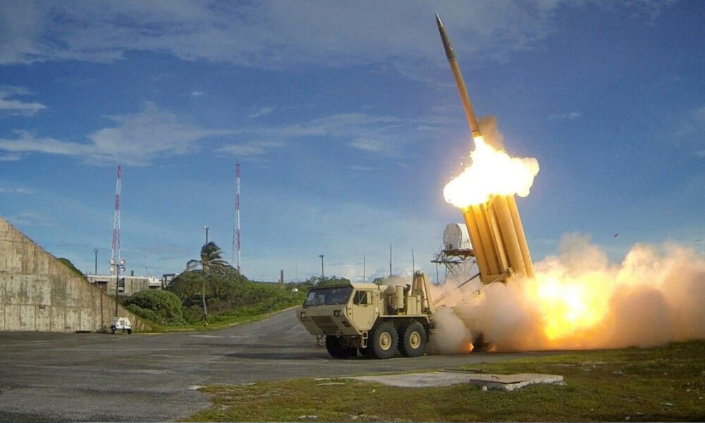 Missile being launched from a mobile launcher on a test range, with bright exhaust plume and smoke at the moment of liftoff.