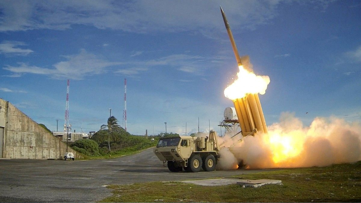 Missile being launched from a mobile launcher on a test range, with bright exhaust plume and smoke at the moment of liftoff.