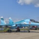 Blue military fighter jet on display at an air show, tail marked with a red star and number 18, canopy closed.