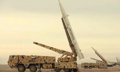 Camouflaged military trucks in a desert with large missiles mounted on launch rails, ready for launch.