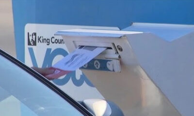 Hand inserting a letter into a blue curbside mailbox labeled King County.
