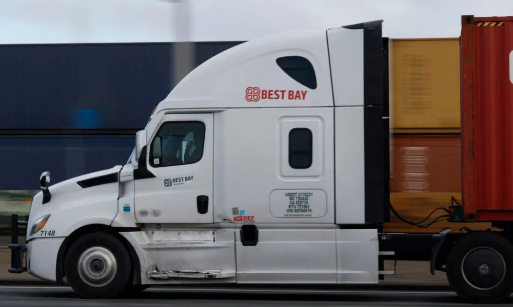 White semi-truck tractor with Best Bay logo pulling a red shipping container on a highway.