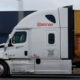 White semi-truck tractor with Best Bay logo pulling a red shipping container on a highway.
