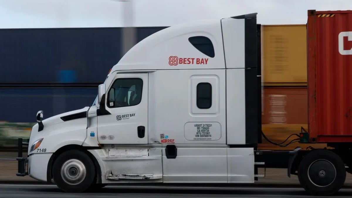 White semi-truck tractor with Best Bay logo pulling a red shipping container on a highway.