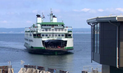 White and green passenger ferry approaching a pier, with the rear loading ramp open and vehicles visible on deck