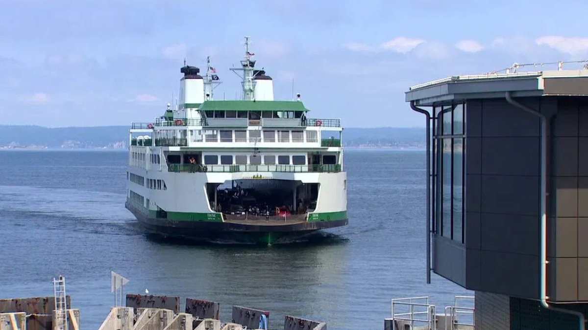 White and green passenger ferry approaching a pier, with the rear loading ramp open and vehicles visible on deck