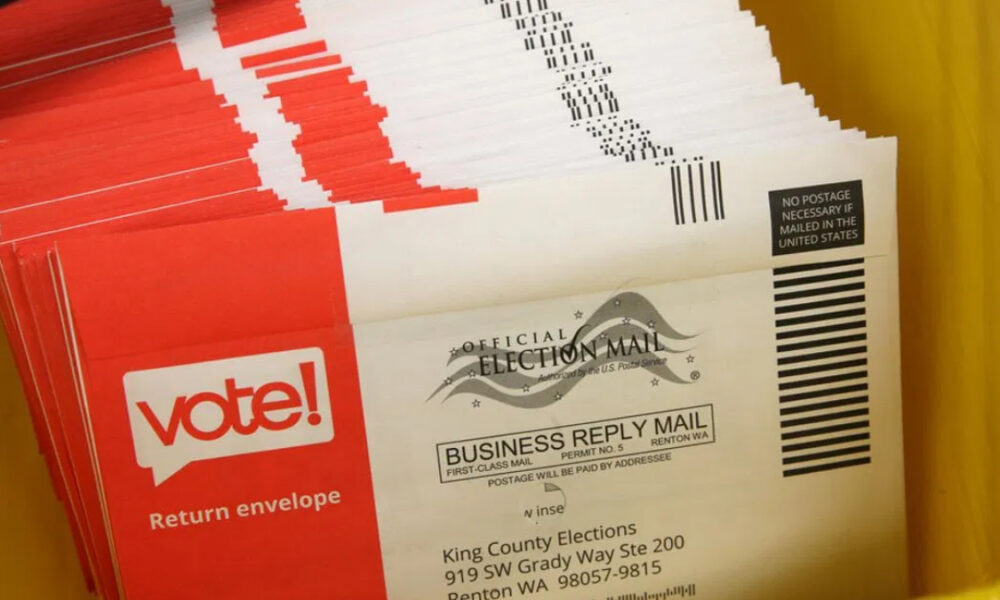 Pile of red and white envelopes labeled 'vote!' for return envelopes, election mail.