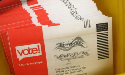 Pile of red and white envelopes labeled 'vote!' for return envelopes, election mail.