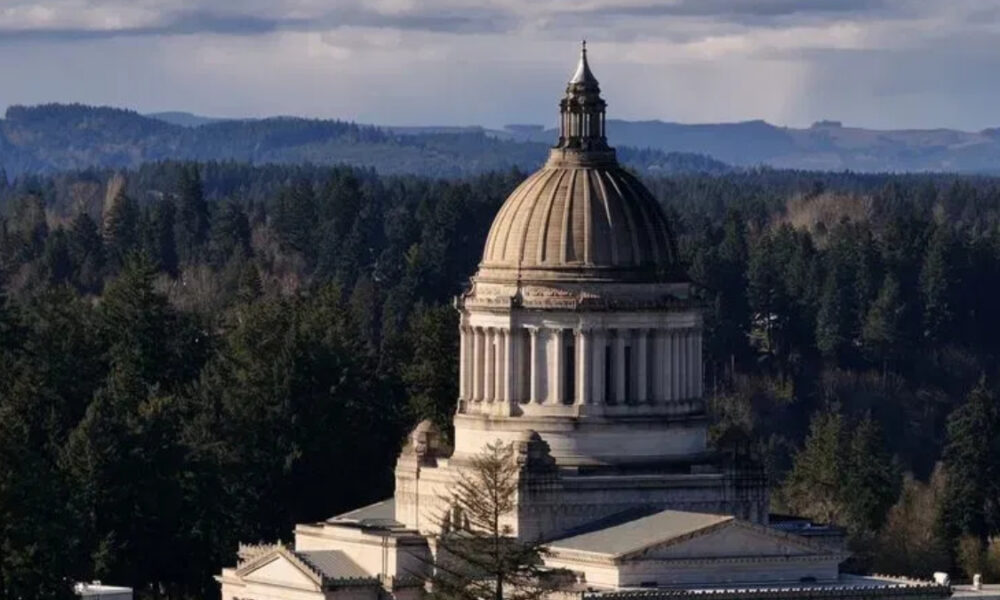 Neoclassical capitol dome rising above trees with distant hills in the background.