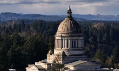 Neoclassical capitol dome rising above trees with distant hills in the background.