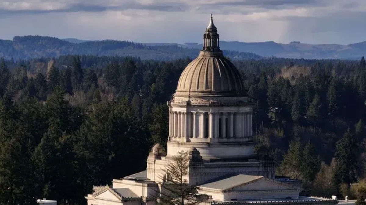 Neoclassical capitol dome rising above trees with distant hills in the background.