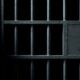 Close-up of dark metal prison bars with a small square access panel and a keyhole on the right side.
