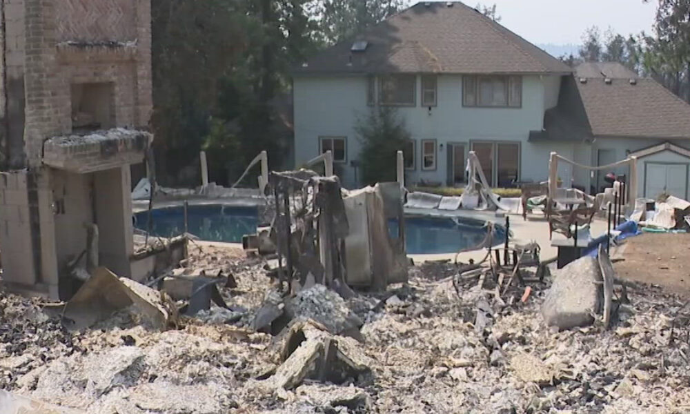 Rubble-filled backyard with a damaged brick structure and a curved swimming pool, a two-story house behind.