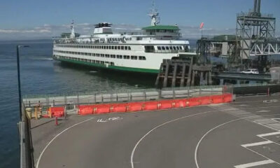White passenger ferry docked at a pier with orange safety barriers along a curved road in the foreground.