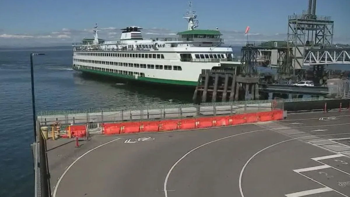 White passenger ferry docked at a pier with orange safety barriers along a curved road in the foreground.