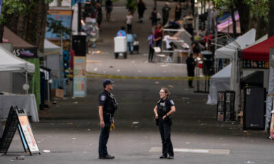Two police officers standing and talking in the middle of a closed street market, with vendor tents and bystanders in the background.