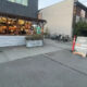 Outdoor restaurant patio with string lights and customers inside, bikes parked along the side, and a chalkboard sign outside offering beer