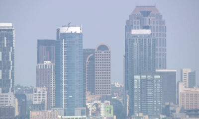 Blue-tinted city skyline with several tall glass office towers against a hazy sky.