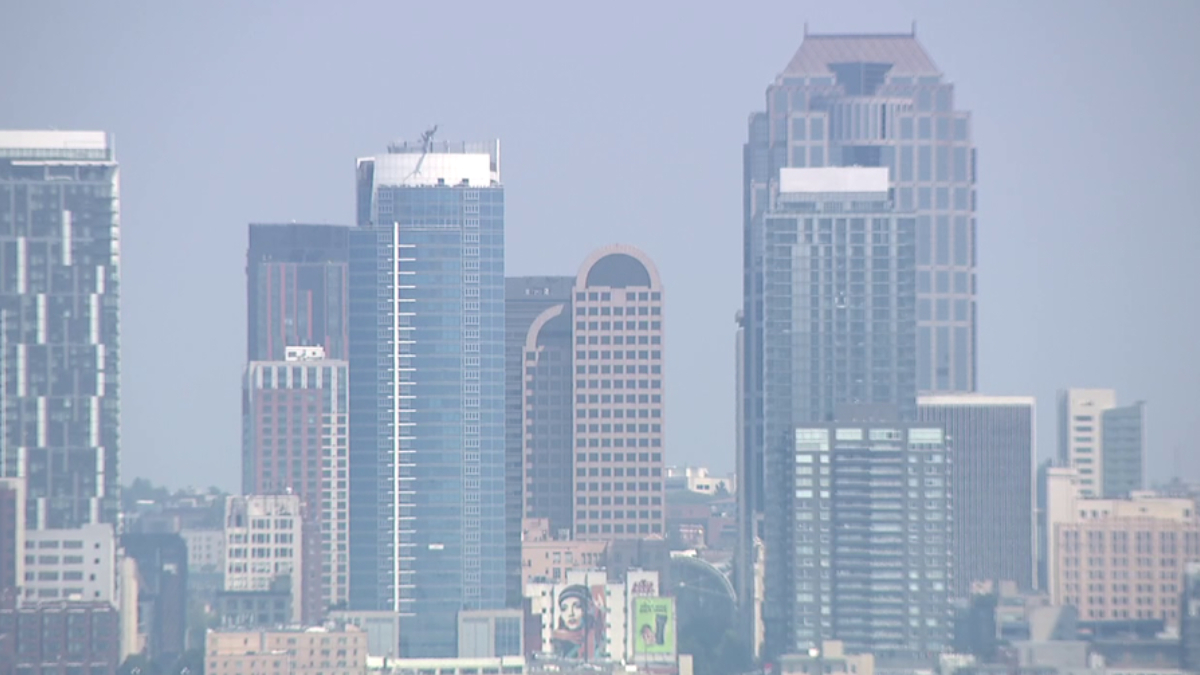 Blue-tinted city skyline with several tall glass office towers against a hazy sky.