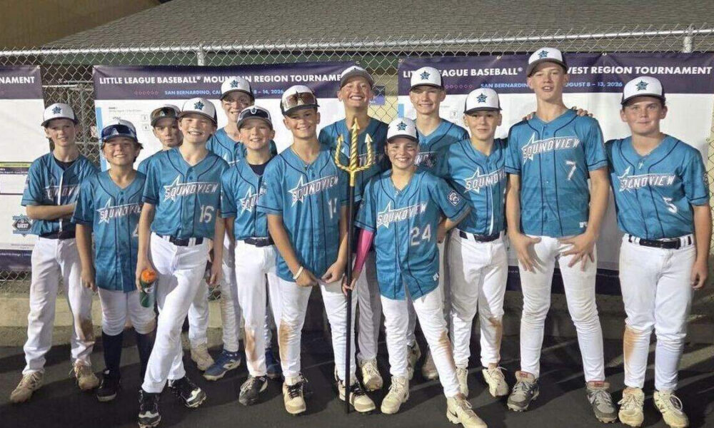 Group of young baseball players in blue uniforms posing with a trophy outdoors at a tournament.