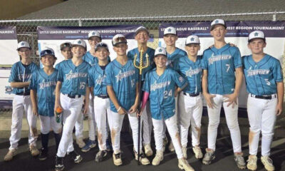 Group of young baseball players in blue uniforms posing with a trophy outdoors at a tournament.