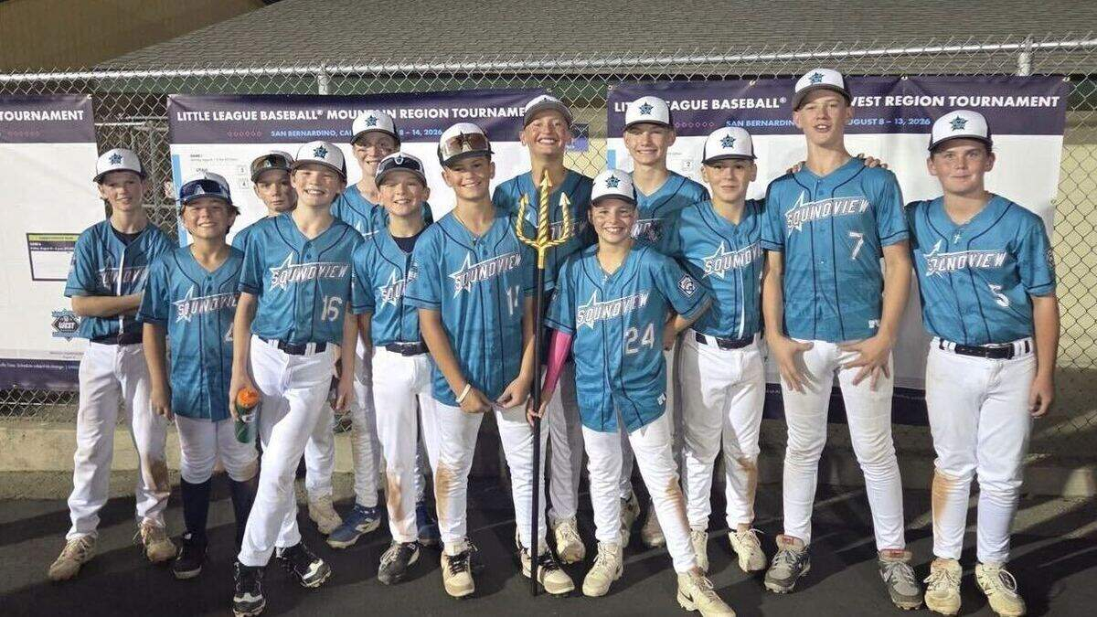 Group of young baseball players in blue uniforms posing with a trophy outdoors at a tournament.