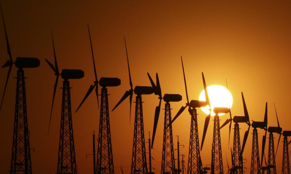 Row of wind turbines silhouetted against an orange sunset sky.